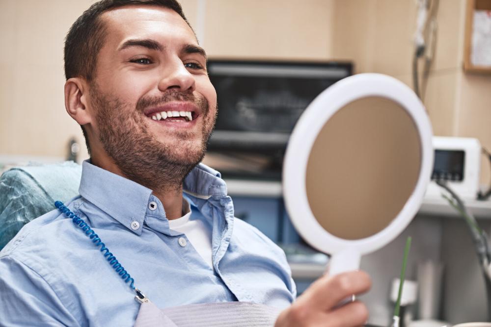 man looking into mirror after dental cleaning in woodland hills