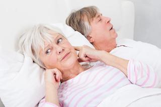 woman sticking fingers in ears while husband snores next to her
