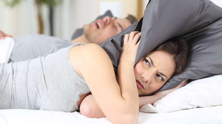woodland hills woman holding pillow over her ears while man snores behind her