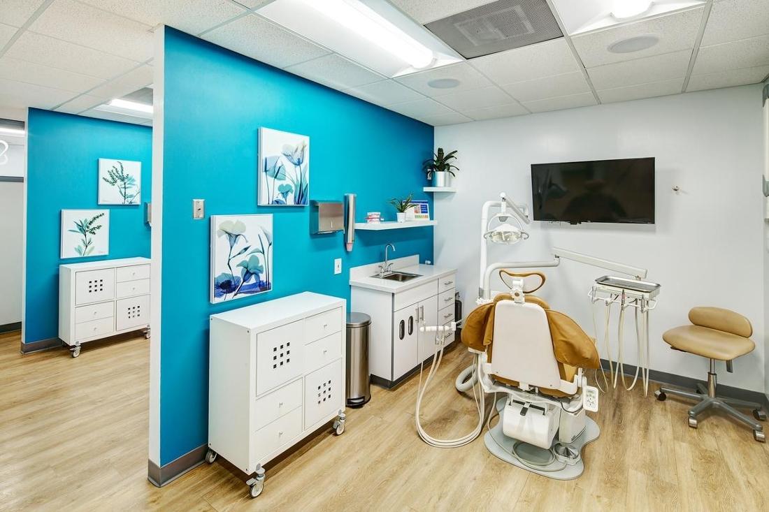 Dental chair in exam room with bright blue wall and tv for patients